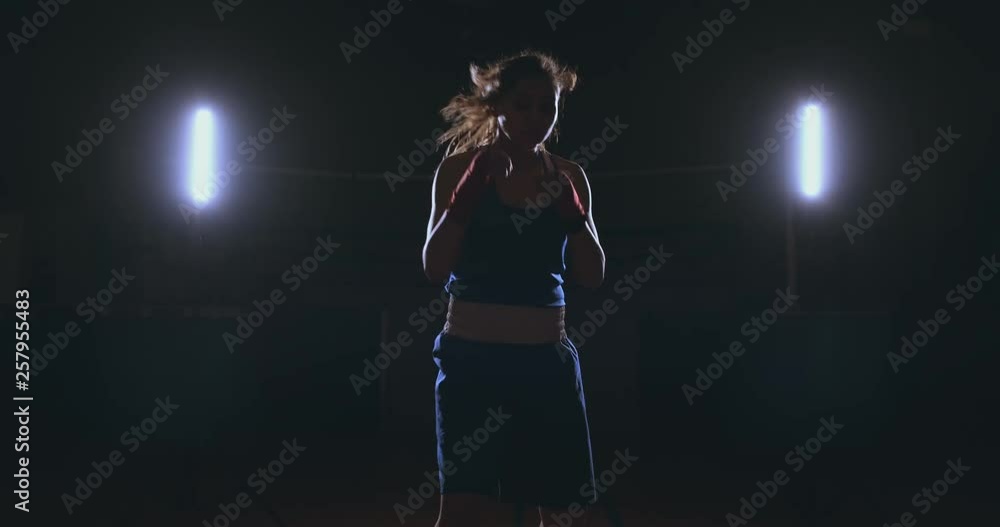 Looking into the camera a beautiful female boxer strikes against a dark background with a backlit light. Steadicam shot Looking into the camera a beautiful female boxer strikes against a dark background with a backlit light. Steadicam shot