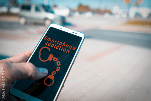 Hands using a smartphone with handcuffs and smartphone addiction words on screen. Internet addiction disorder, IAD, and Mobile phone overuse or smartphone addiction concept. photo