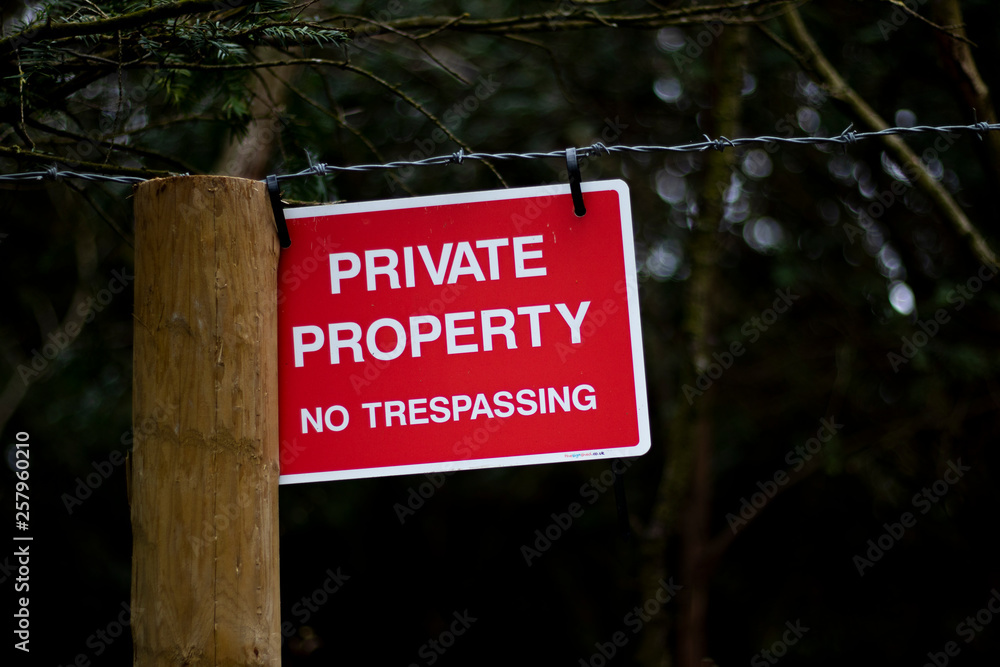 Private property no trespassing sign fixed to barbed wire fence protecting woodland with shallow depth of field Private property no trespassing sign fixed to barbed wire fence protecting woodland with shallow depth of field