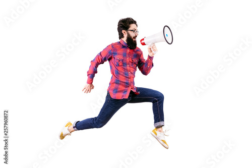 full length studio portrait of bearded hipster man in glasses, jumping and shouting in megaphone, isolated on white background