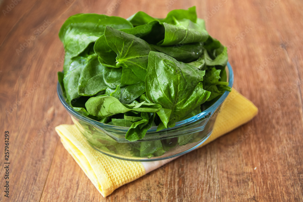Fresh raw organic spinach leaves in a glass bowl on rustic wooden table Fresh raw organic spinach leaves in a glass bowl on rustic wooden table