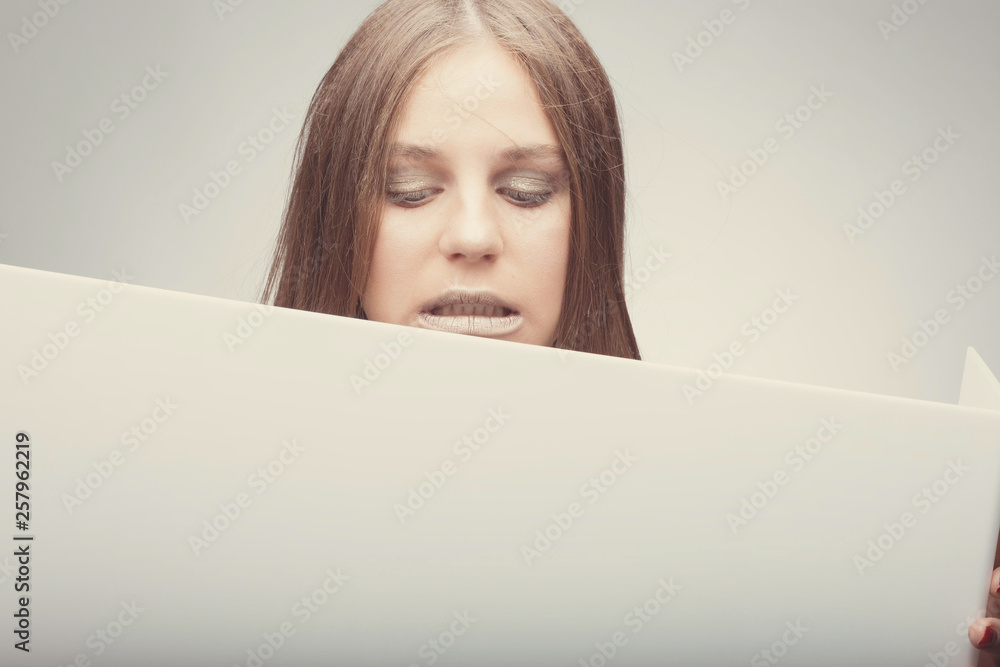 Fashion pretty girl holding white board with place for text. Surprised girl looking confused Fashion pretty girl holding white board with place for text. Surprised girl looking confused