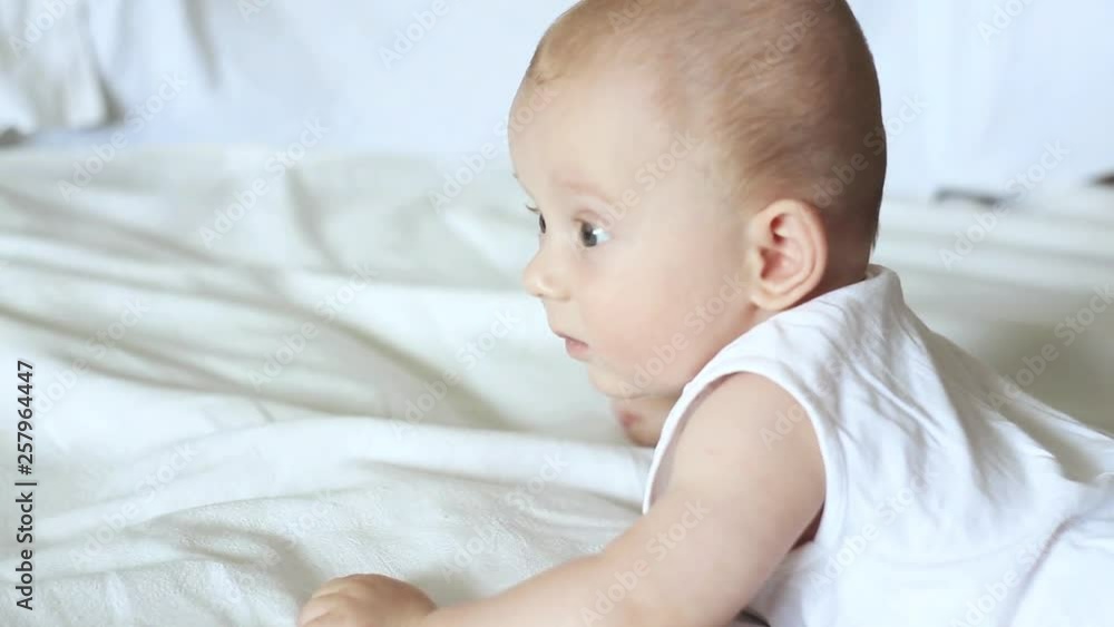 Cute happy 6 month baby boy lying and playing on a white bed Cute happy 6 month baby boy lying and playing on a white bed
