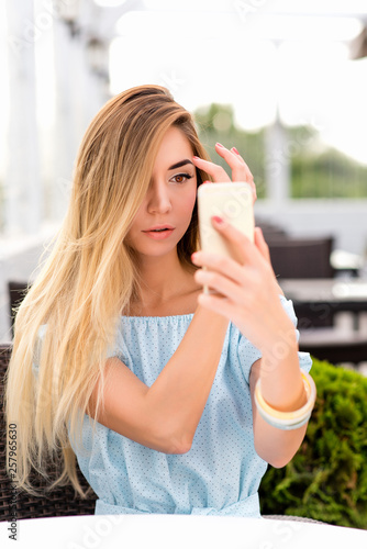 A girl in a cafe adjusts her hair long hair, in her hand a mobile phone, a pocket mirror, a front camera. Looks makeup. Video call, online application to the Internet, video chat.