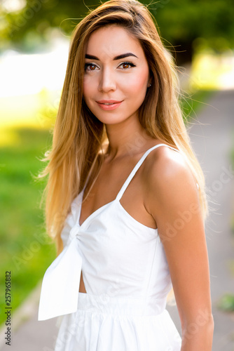 Fototapeta Naklejka Na Ścianę i Meble -  Beautiful and happy girl in white dress, long hair, close-up in the summer in the city outdoors. Emotions joy fun holiday, walk in the park lifestyle.