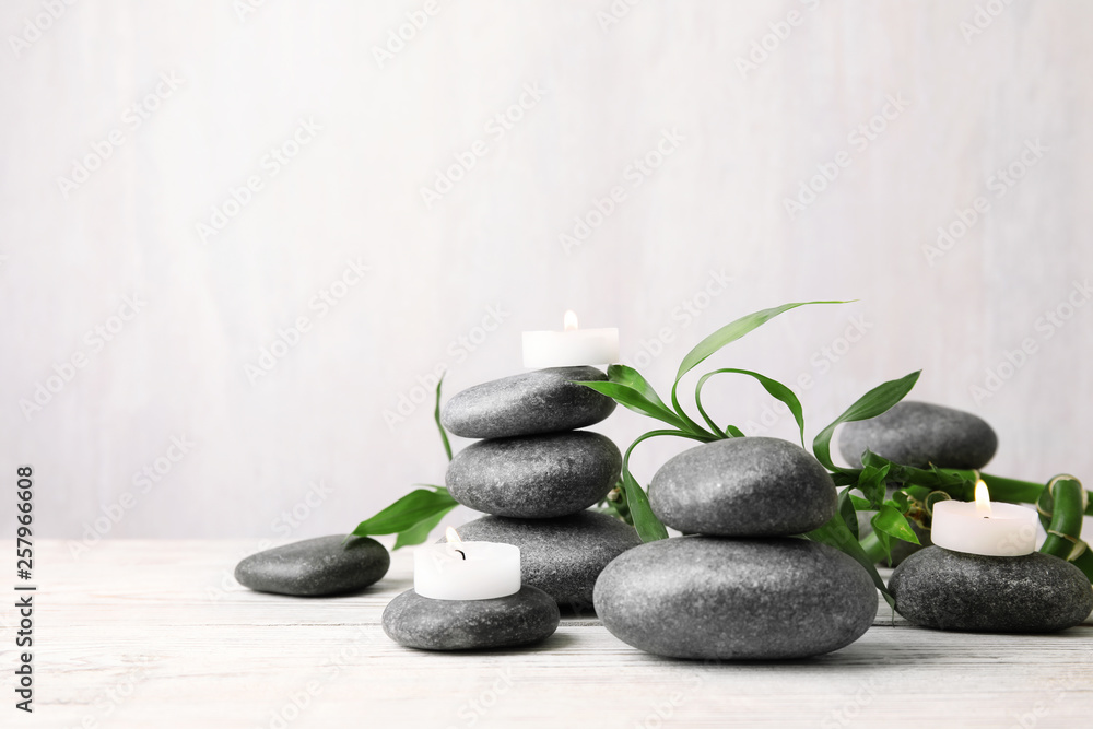 Composition with zen stones, bamboo and lighted candles on table against light background. Space for text Composition with zen stones, bamboo and lighted candles on table against light background. Space for text