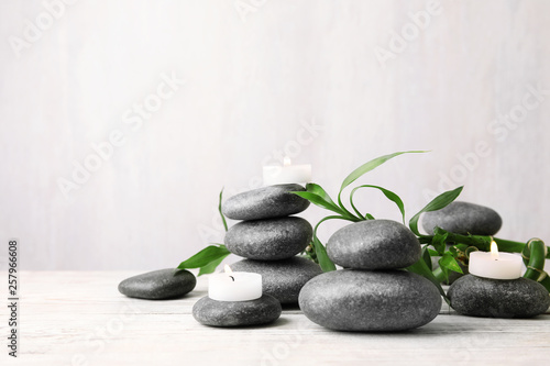Composition with zen stones, bamboo and lighted candles on table against light background. Space for text