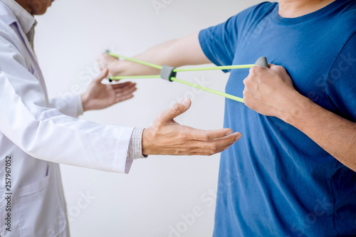 Doctor physiotherapist assisting a male patient while giving exercising treatment on stretching his arm with exercise band in the clinic, Rehabilitation physiotherapy concept