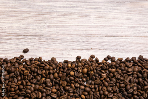 Roasted coffee beans in bulk on a light wooden background. dark cofee roasted grain flavor aroma cafe, natural coffe shop background, top view from above, copy space