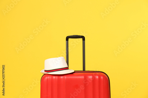 Bright suitcase with hat on color background