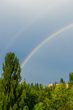 Natural double rainbow over green trees, summer city landscape