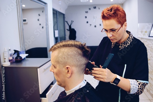 Woman hairdresser cutting male customer hair with electric trimmer.