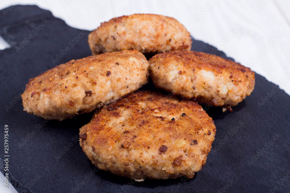 cutlets on a black flat plate, on a white wooden background