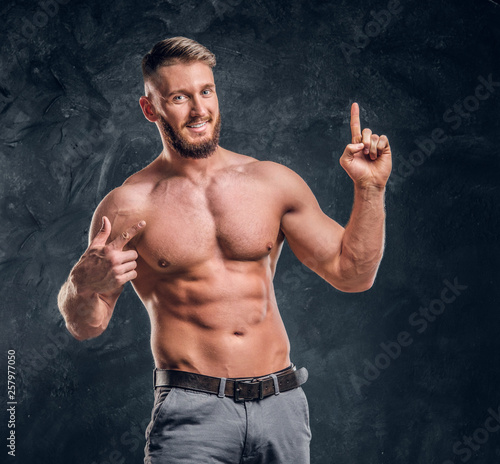 Cheerful shirtless man with the muscular body posing for a camera. Studio photo against dark wall background