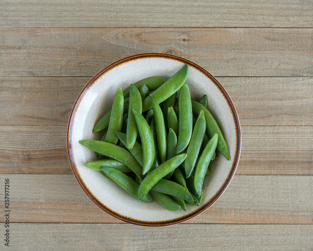 a small bowl of green sugar snap peas on a wood background viewed from above a small bowl of green sugar snap peas on a wood background viewed from above
