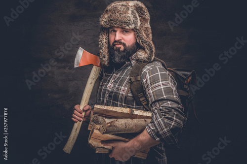 Brutal woodcutter with firewood and ax. Studio photo against a dark textured wall photo