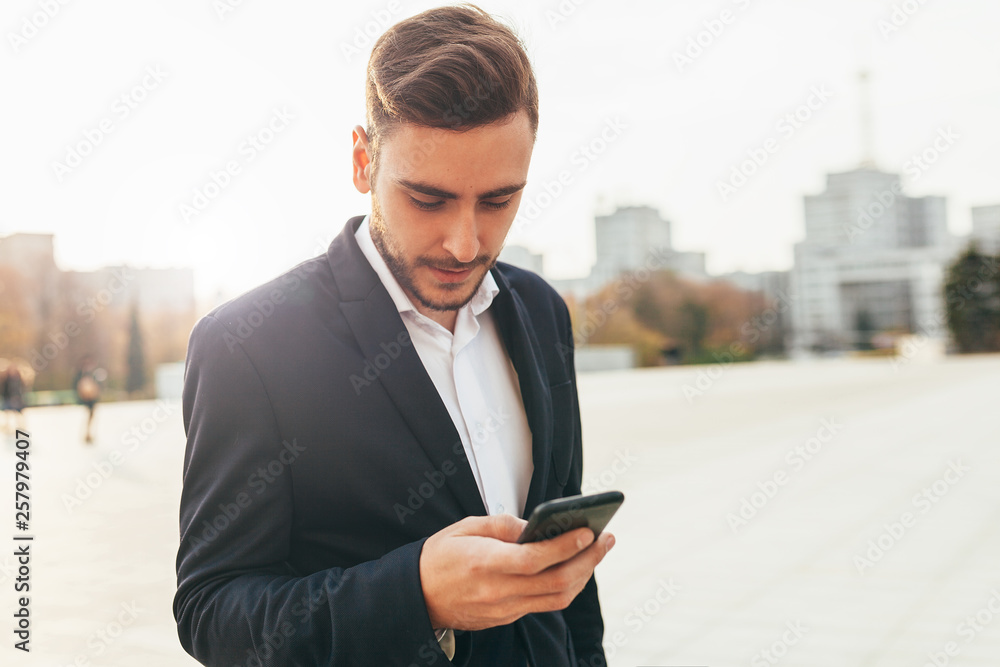 Millennial businessman looks into the screen of his mobile phone. Close-up portrait. Young successful, stylish business man walks on a city street, watching social networks in his smartphone Millennial businessman looks into the screen of his mobile phone. Close-up portrait. Young successful, stylish business man walks on a city street, watching social networks in his smartphone