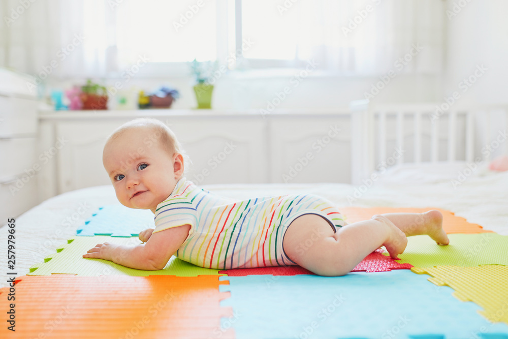 baby girl lying on colorful play mat on the floor baby girl lying on colorful play mat on the floor