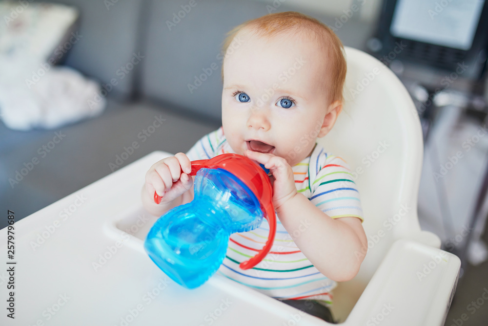 Little baby girl sitting in high chair and drinking water from sippy cup Little baby girl sitting in high chair and drinking water from sippy cup
