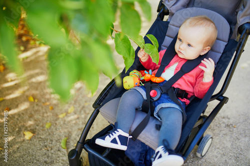 Adorable baby girl sitting in stroller and looking at leaves on a fall or spring day in park