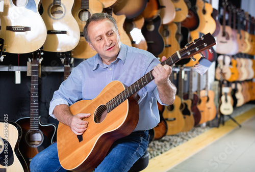 Adult guitarist is playing on acoustic guitar in music store. photo