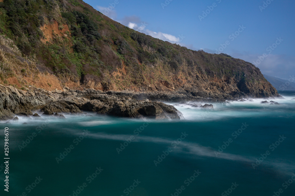 Long exposure of deep blue water, swirling surf, and rocky cliffs of central California