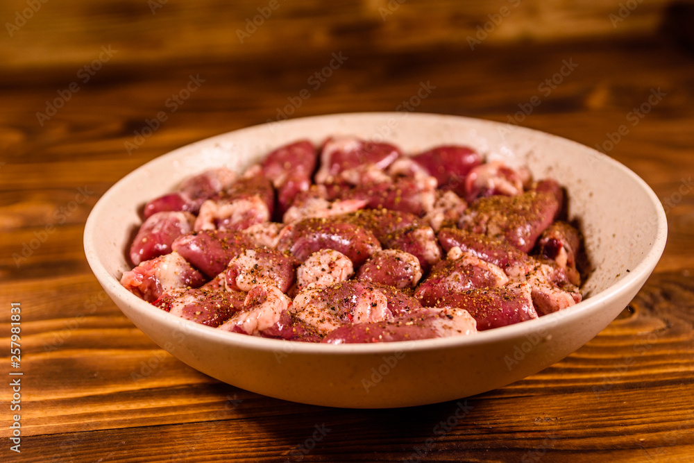 Ceramic plate with raw chicken hearts on wooden table Ceramic plate with raw chicken hearts on wooden table