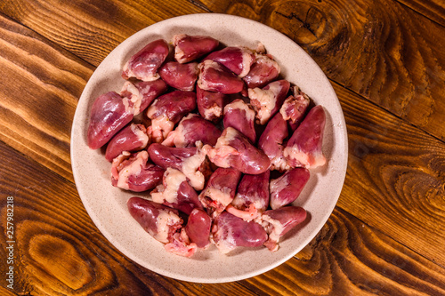 Ceramic plate with raw chicken hearts on wooden table. Top view