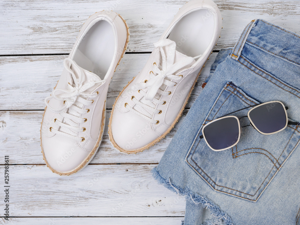 Womens clothing, shoes, accessories (white sneakers, denim shorts, sunglasses). Fashion outfit, spring summer collection. Shopping concept. Flat lay, view from above