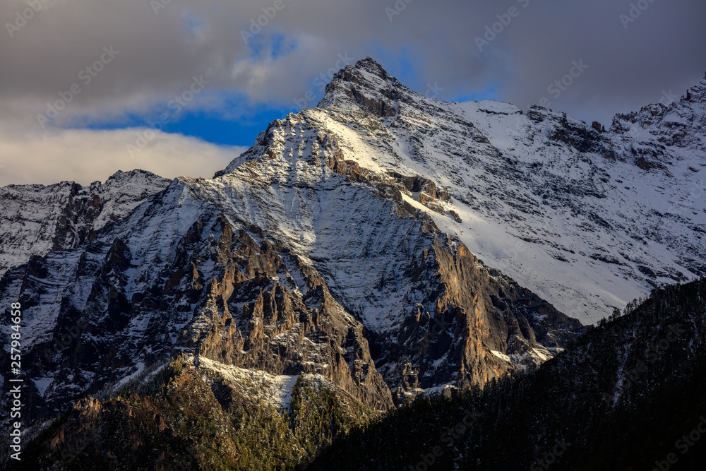 Snow mountains, epic snow covered mountain range - Daocheng Yading Nature Reserve. Ganzi, Garze, Kham Tibetan area of Sichuan Province China. Dramatic lighting during sunset, Clouds and Sky