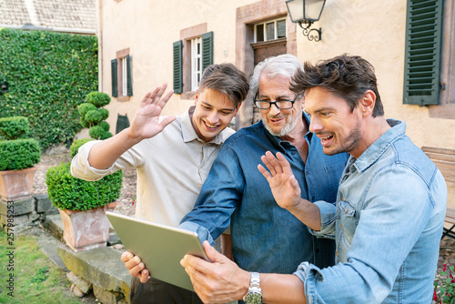 Three men of different age having a video chat via tablet in garden photo