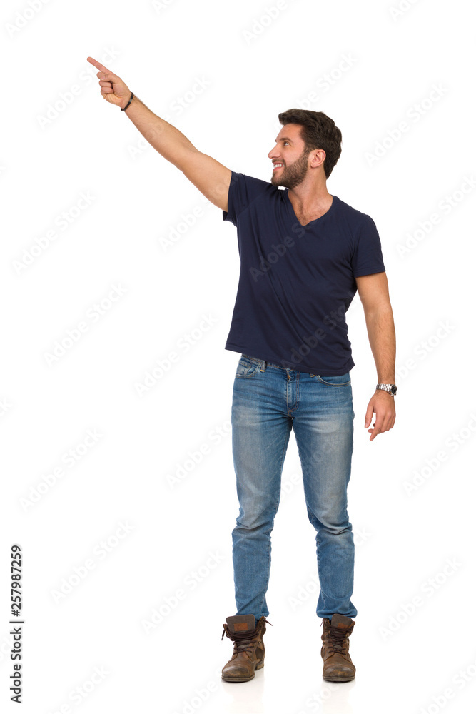 Smiling Handsome Man In Jeans T-Shirt And Boots Is Pointing Up And Looking Away Smiling Handsome Man In Jeans T-Shirt And Boots Is Pointing Up And Looking Away