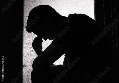Photography silhouette of young man feeling sad, tired sitting in a dark room