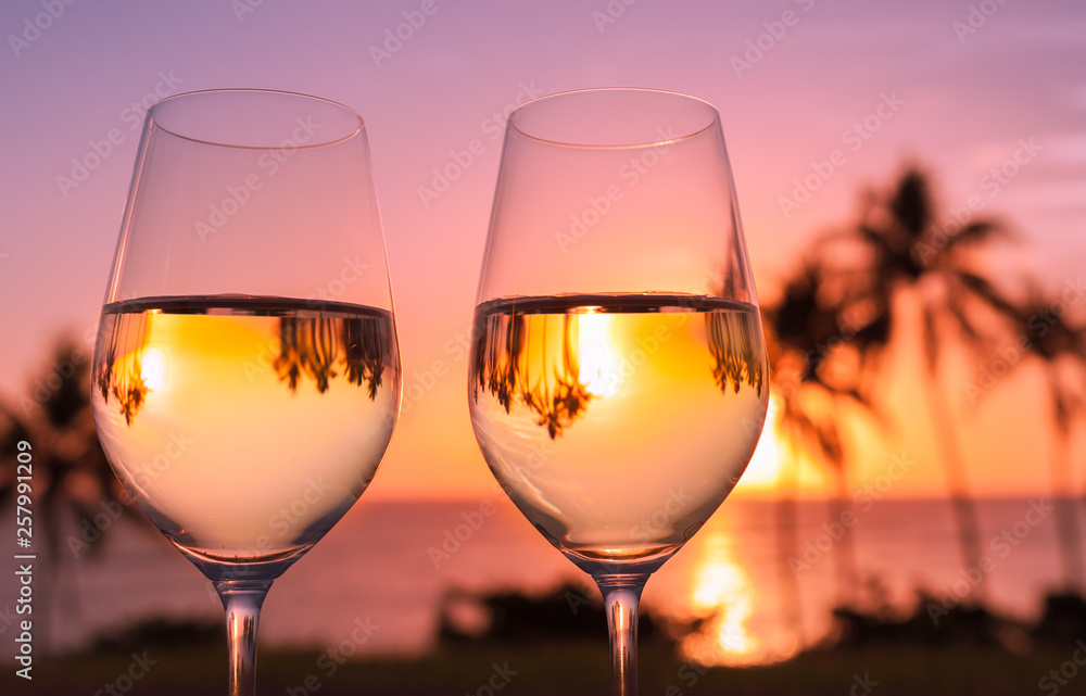 Pair of wine glasses for two against tropical sunset background 