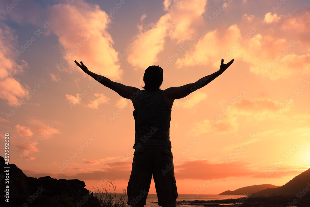 silhouette of man with arms up feeling happy and free on top of mountain