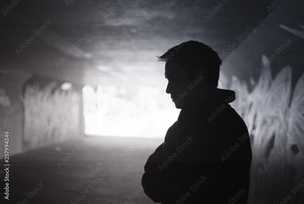 Depressed sad young man standing in a dark city tunnel  - obrazy, fototapety, plakaty 