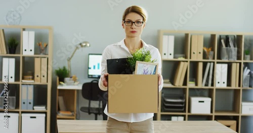 Portrait shot of the Caucasian sad blond woman stannding in the office with a box full of stuff after being fired. Inside. photo