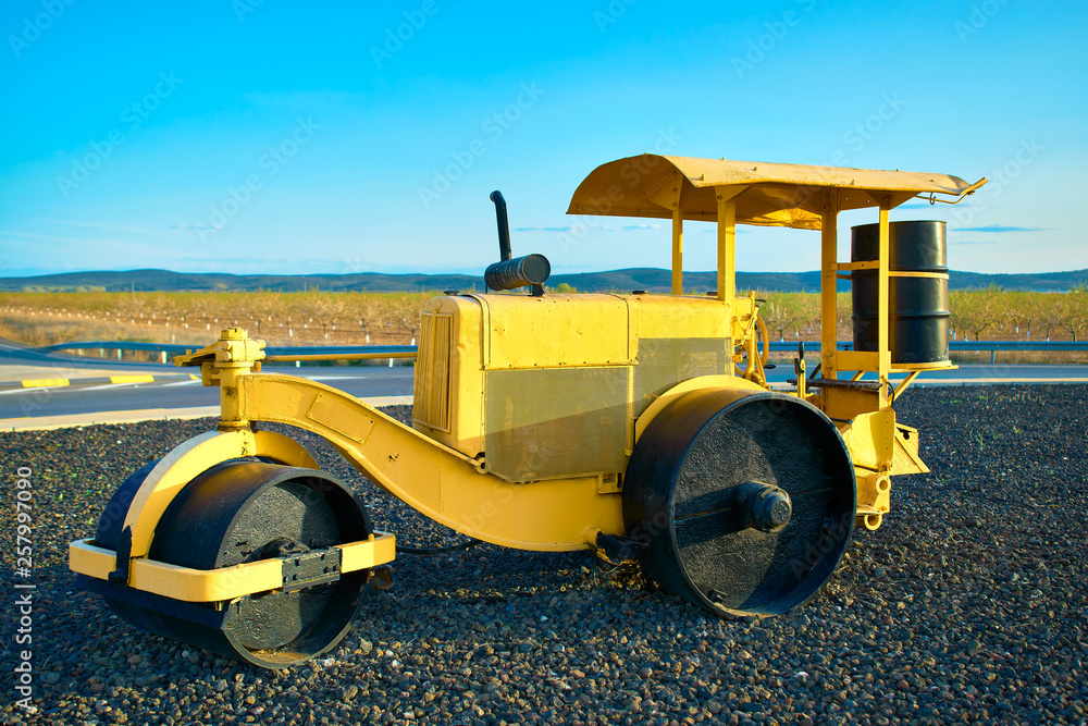 Naklejka premium Selective focus diagonal view of and old classic yellow steamroller / road roller used as decoration in a roundabout of a highway in Spain
