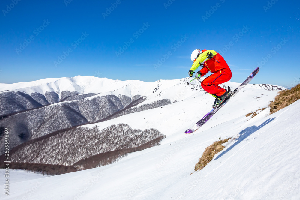 A skier is riding and jumping at mountain terrain. A wonderful sunny day