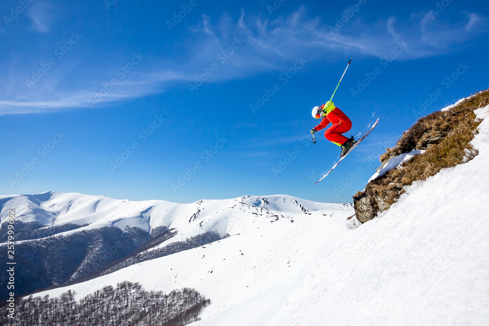 A skier is riding and jumping at mountain terrain. A wonderful sunny day