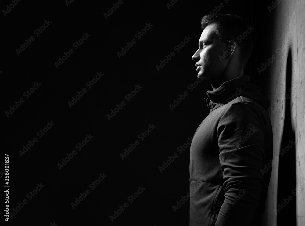 Young athletic man grey sport wear is near concrete wall with shadow on it Young athletic man grey sport wear is near concrete wall with shadow on it
