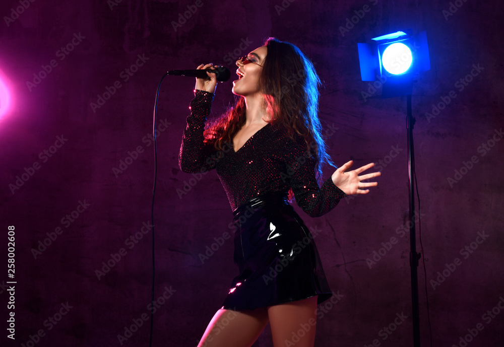 Beautiful singing girl curly afro hair singer sing with microphone karaoke song on stage on dark neon light Beautiful singing girl curly afro hair singer sing with microphone karaoke song on stage on dark neon light