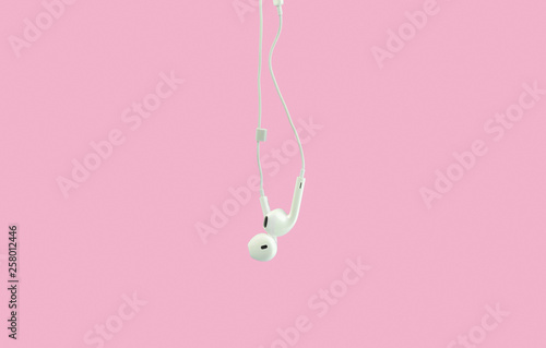 White hanging ear buds headphones isolated on a pink background photo