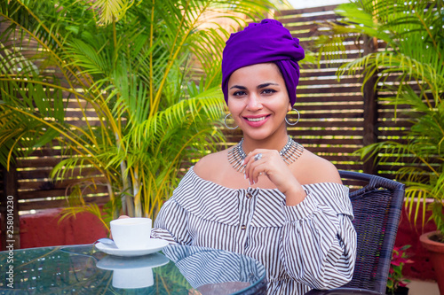 Fashion afro american girl with ethnic turban on head culture coffeebreak at summer tropical cafe . indian woman drinking tea photo