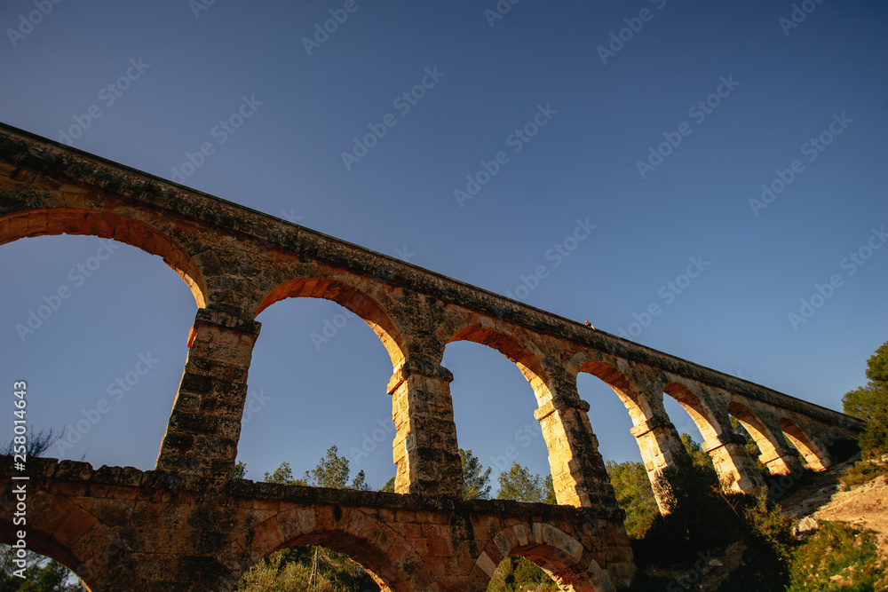 Rebellious traveling woman sitting on ancient monument. Roman Aqueduct El Pont del Diable in Tarragona, Spain