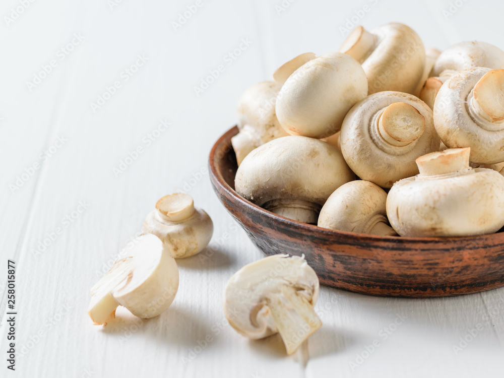 Sliced mushrooms next to a bowl of mushrooms on a white table. Vegetarian cuisine.