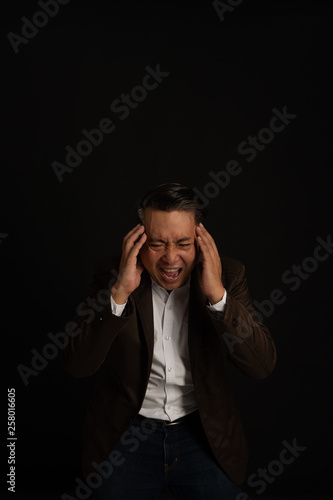depressed man sitting head in hands  and scream  in the dark  with low light in studio; dramatic concept; Free from copy space.