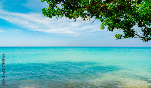 Beautiful tropical paradise beach background. Summer vibes. Summer vacation time background. Ocean waves. Calm, tranquil and relax scene. Emerald green sea water and blue sky and white clouds. Skyline