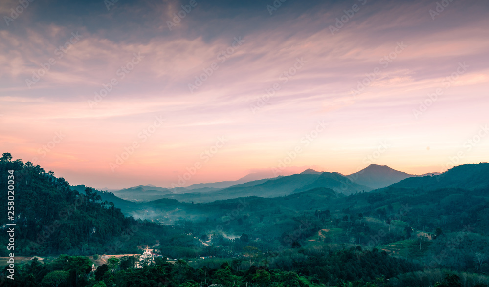 Beautiful nature landscape of mountain range with sunset sky and clouds. Rural village in mountain valley in Thailand. Scenery of mountain layer at dusk. Tropical forest. Natural background.