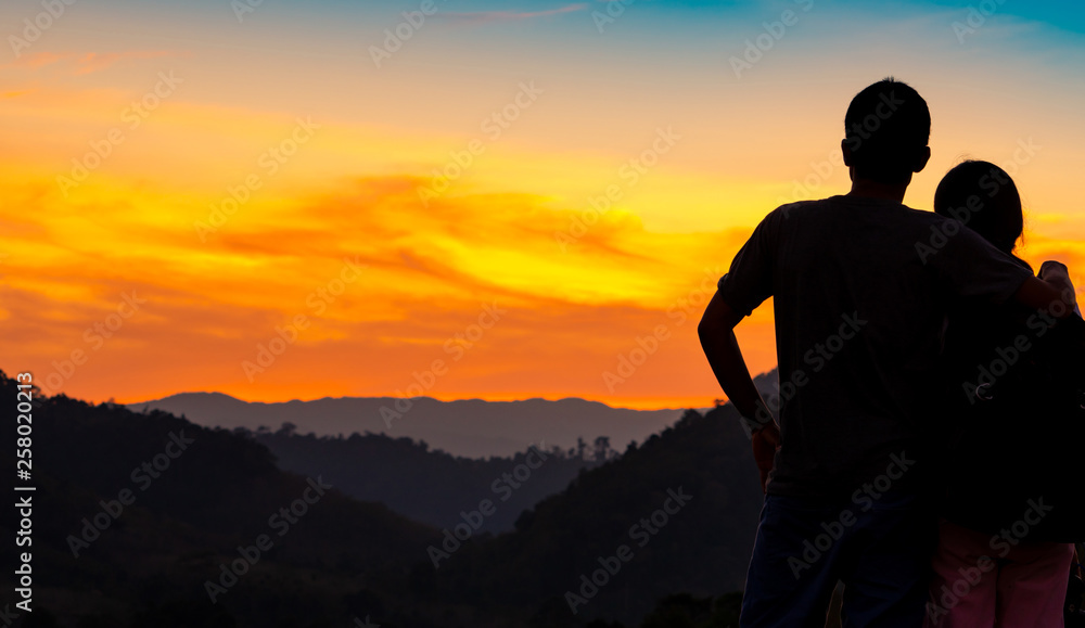 Back view of romantic couple watching beautiful sunset over mountain layer. Couple travel. Backpacker happy in love and travelling honeymoon. Silhouette of two tourist hiking to top of mountain.